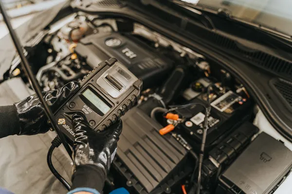 Un appareil de diagnostic tenu près du compartiment moteur d’une voiture à l’arrêt