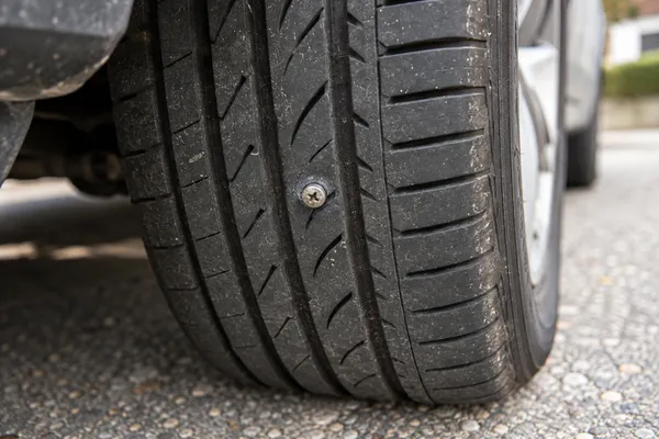 Une vis plantée dans la bande de roulement d’un pneu de voiture immobilisée.