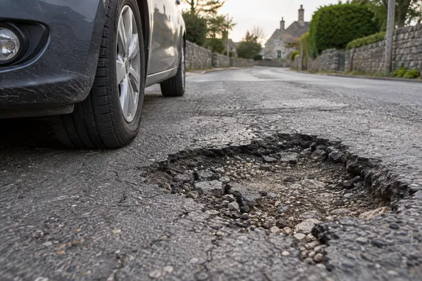Un nid-de-poule dans la chaussée près d’une roue de voiture à l’arrêt.
